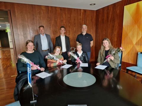 Female athletes sit at a table with grants and flowers, with three men standing behind them in a posed photo.