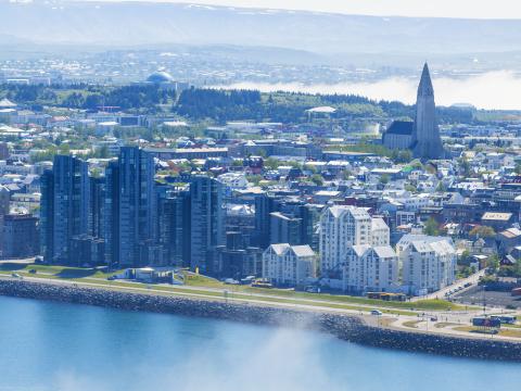 Loftmynd yfir Reykjavík, útsýni frá Sæbraut, yfir miðborg, að Hallrímskirkju og Perlu. Sjór í forgrunni, fjöll og sjór í bakgrunni. Mistur yfir.