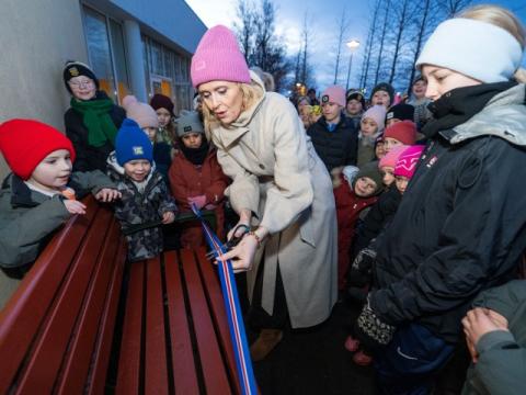 Mayor Heiða Björg Hilmisdóttir dedicates the buddy bench at Engjaskóli by cutting a ribbon as students look on.