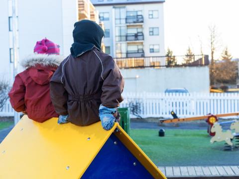 Börn sitja upp á litlum kofa á leikskólalóð.