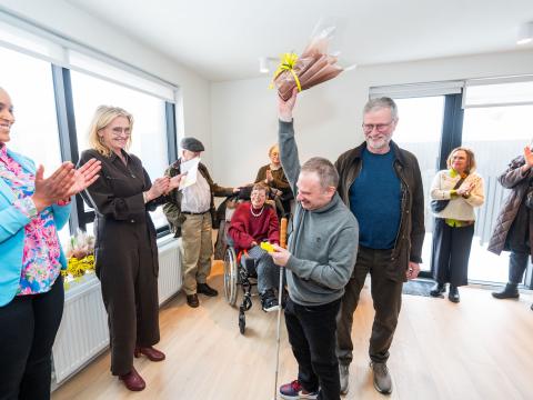 Kjartan Ásmundsson raises a bouquet of flowers like a trophy to celebrate receiving keys to his new home. The mayor and the chair of the Welfare Council also appear in the photo. 
