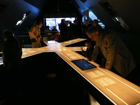Visitors at the Settlement Exhibition on Aðalstræti. A dimly lit space with people gathered around an illuminated scale model of streets.