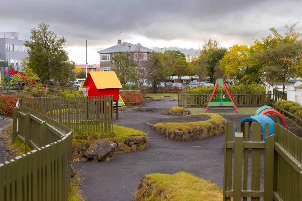 Outdoor play area at Grænaborg preschool where you can see a small house, swings and other playground equipment.