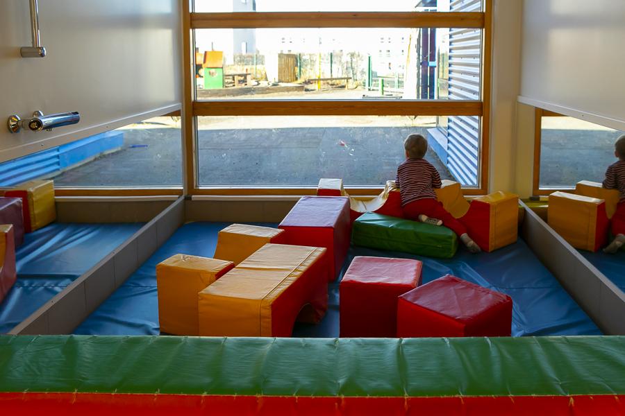Cushion area and a child looking out the window in the Litir building, part of Rauðhóll Preschool