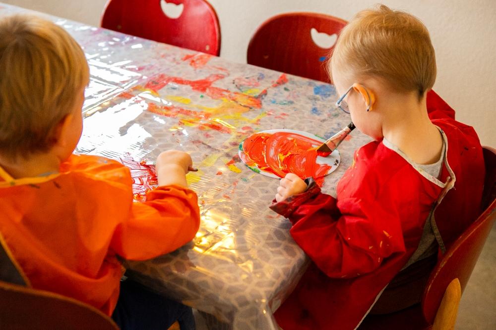 View from behind of children sitting at a table painting at Bjartahlíð preschool