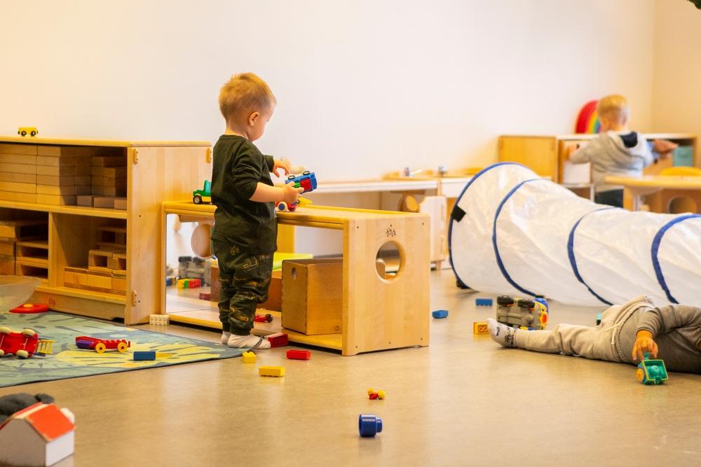 Child playing with a toy car by shelves with toy blocks and other toys at Bjartahlíð preschool