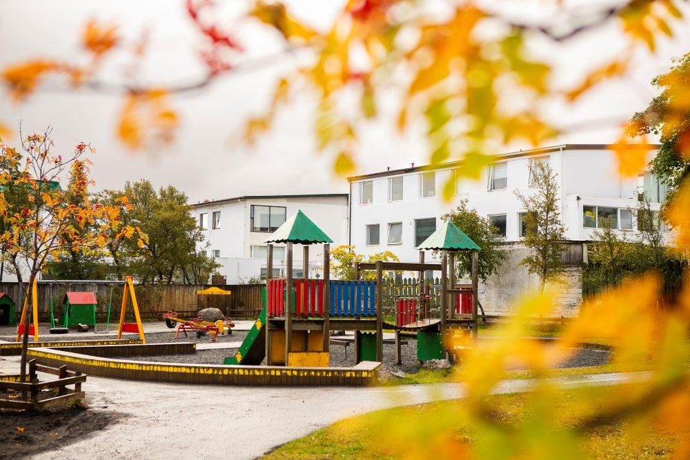Play castle, swings and road salt in the outdoor area at Bjartahlíð preschool. Leaves in the foreground.