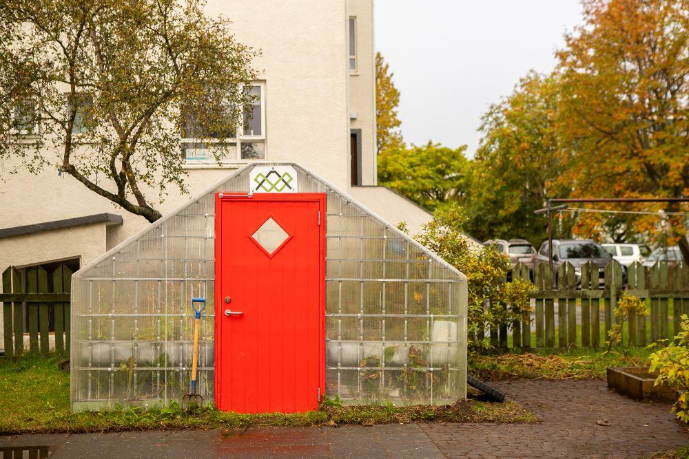The Greenhouse with red door in the outdoor area at Bjartahlíð preschool