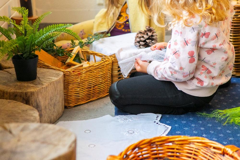 Child sitting on the floor playing with cloths, cones and wooden toys at Bjartahlíð preschool