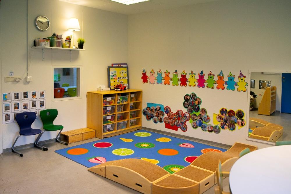 Blue rug with pictures of fruit, toys on shelves and decorated walls at Gullborg Preschool