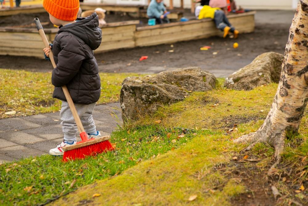 Child dragging a broom behind them in the outdoor area of Gullborg Preschool