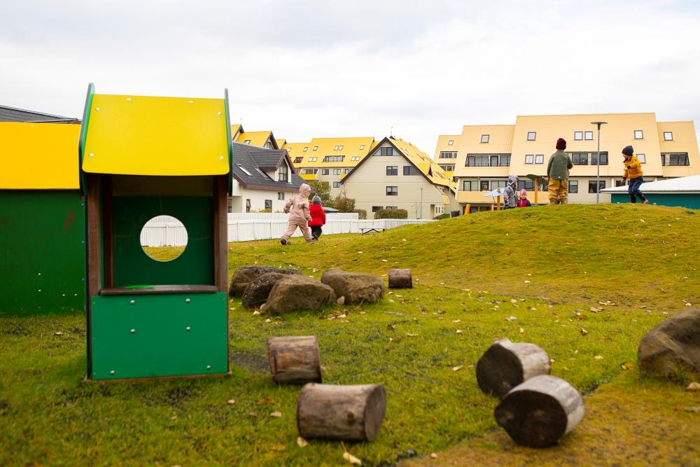 Grass mounds, tree stumps and a small playhouse in the outdoor area of Gullborg Preschool