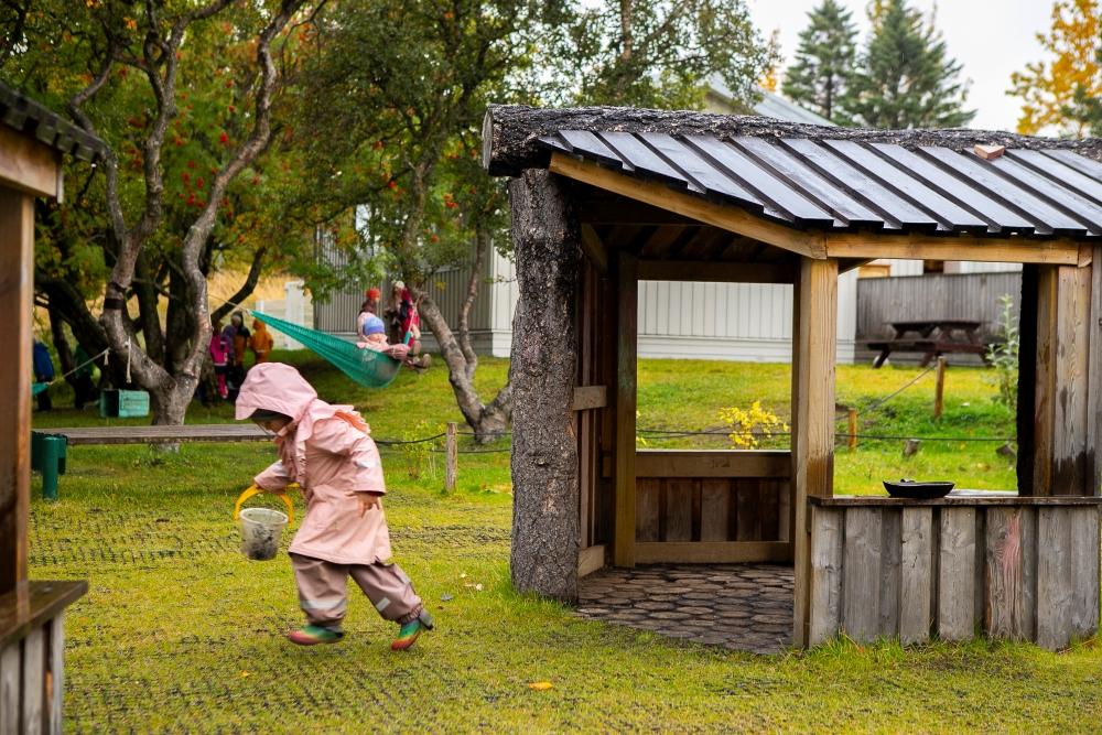 Child in a pink raincoat running away from a small wooden house