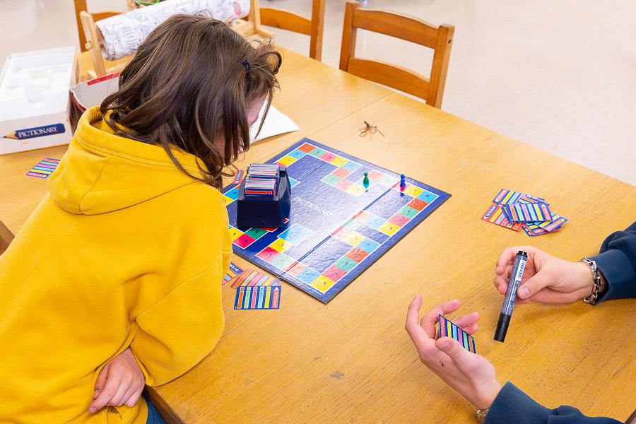 Children sit at table playing cards. 