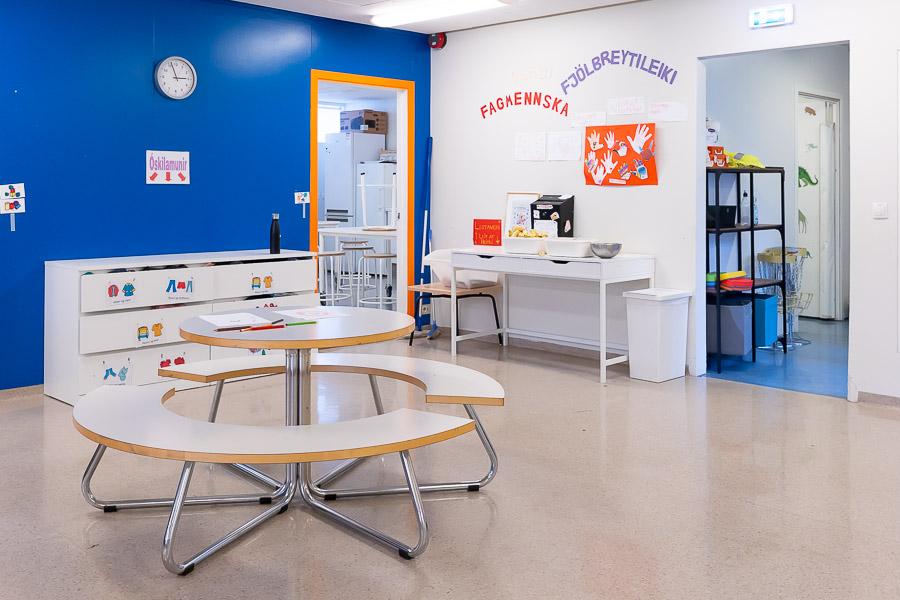 Round table and benches. Blue wall with a clock and a sign that reads "lost and found." White dresser under the sign. 