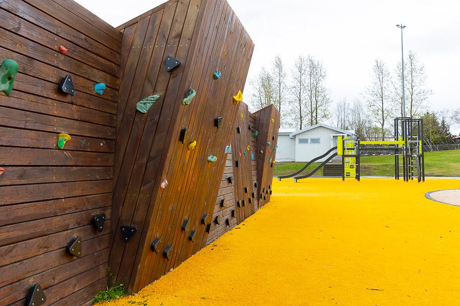 Brown climbing wall on yellow school playground. Playground castle in the background. 