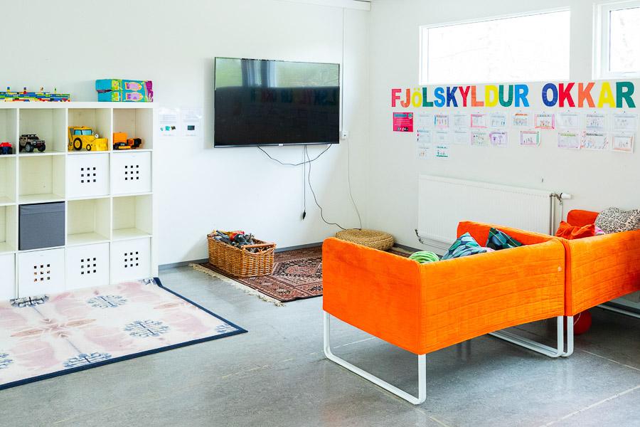 A room at the Dalheimar after-school program featuring an orange sofa, television and shelves filled with toys.