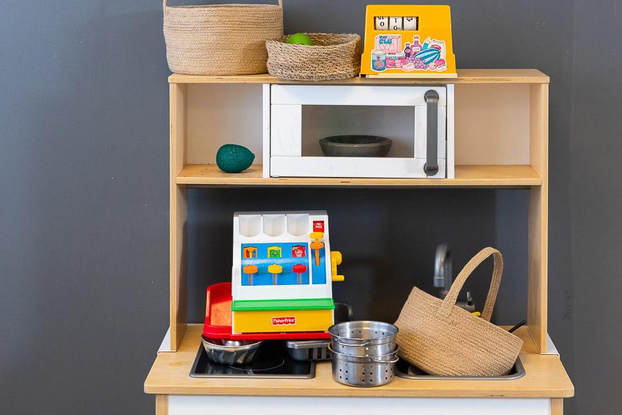 A toy kitchen with a microwave and stovetop along with a toy cash register.