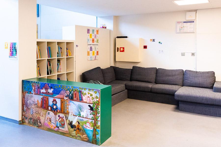 Room at Eldflaugin after-school program with a large gray sofa, bookshelves and decorated back of a bookshelf in the foreground.