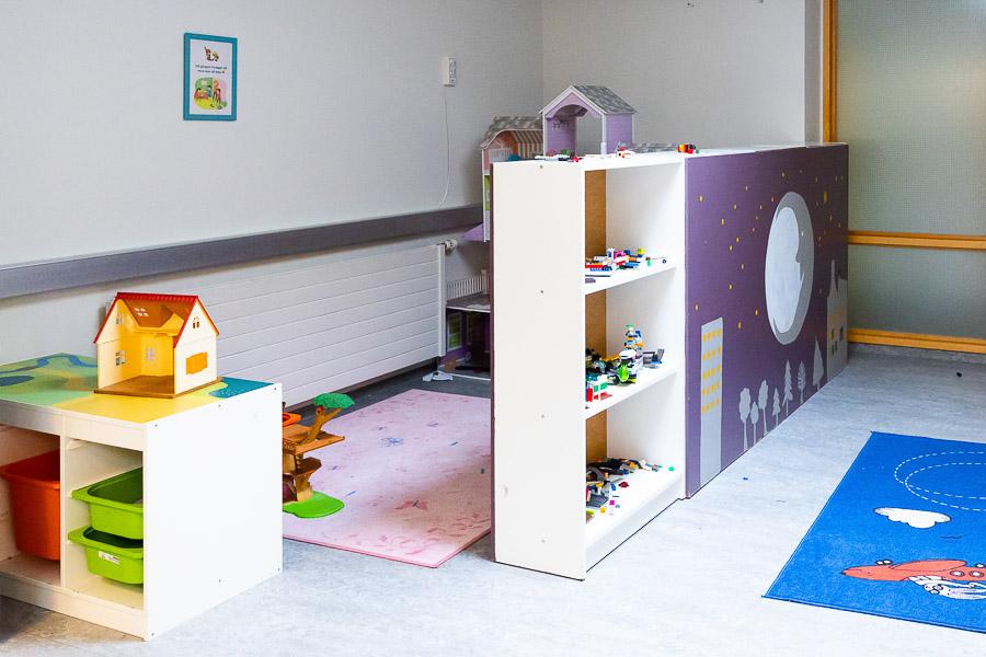 Play area at Eldflaugin after-school program with colorful rugs, shelves with Lego blocks and a dollhouse.