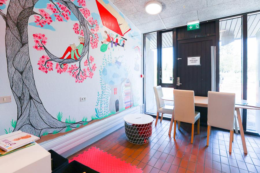 Table and chairs in front of a black door and wall decorated with a large tree.