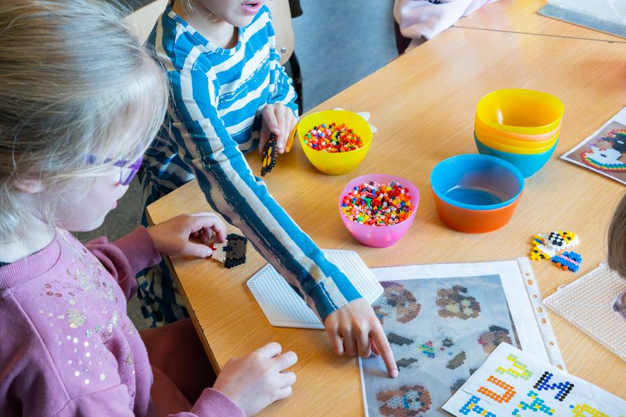 Children sit at a table playing with Perler beads.