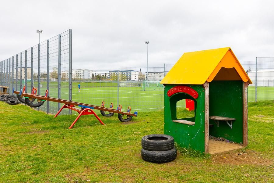 Small green playhouse with yellow roof, road salt and soccer field in the background. 