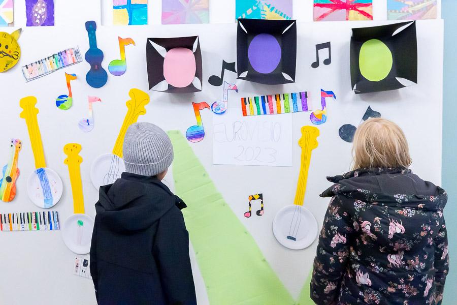 Children in jackets looking at a wall decorated for Eurovision.