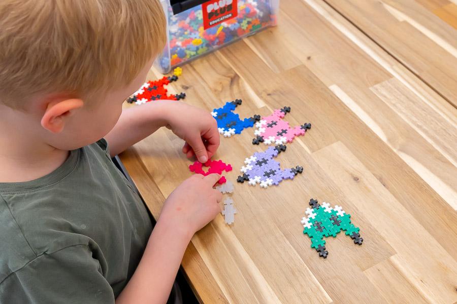 A child sits at a table playing with Perler beads. 
