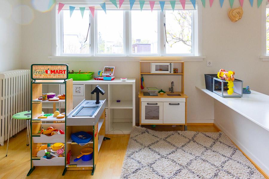 Room with a toy kitchen, rug on the floor and bunting in the window.