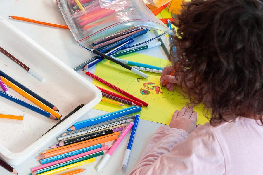Child sits at a table coloring with colored pencils. 