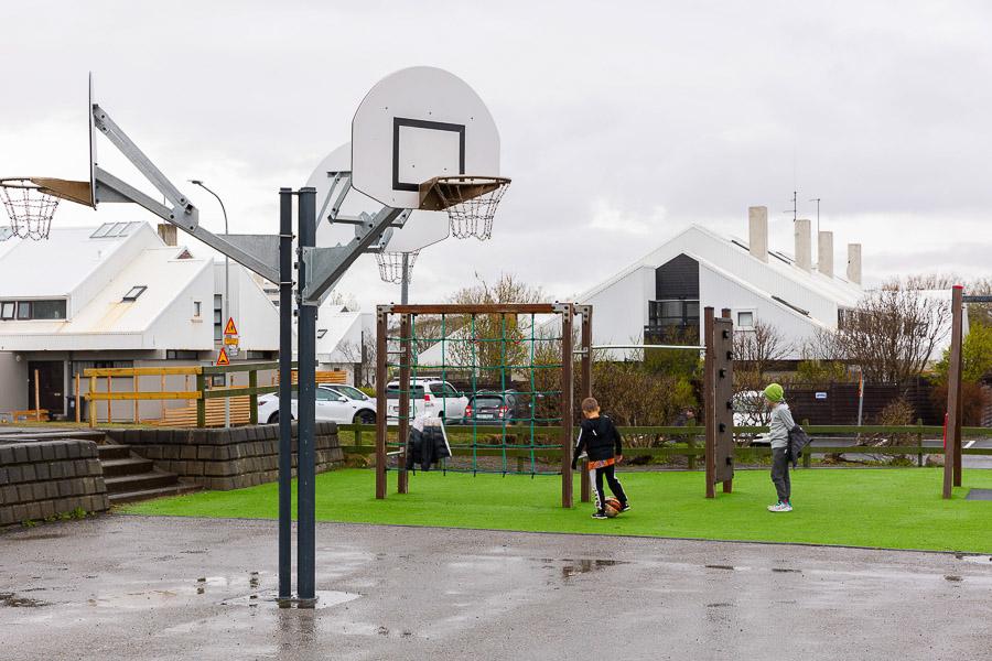 A basketball backboard, jungle gym and children playing soccer.