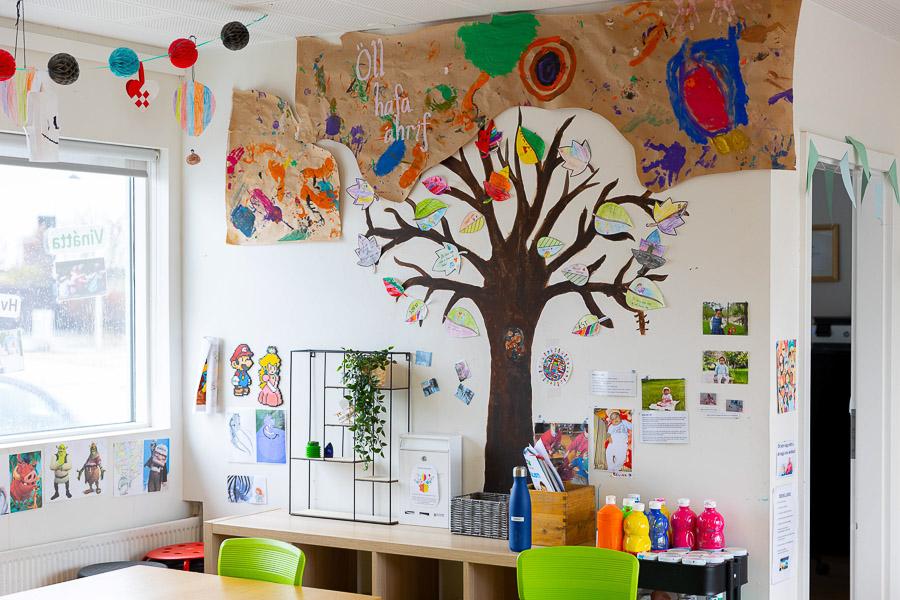 A wall decorated with a large tree, leaves and various artworks by children.