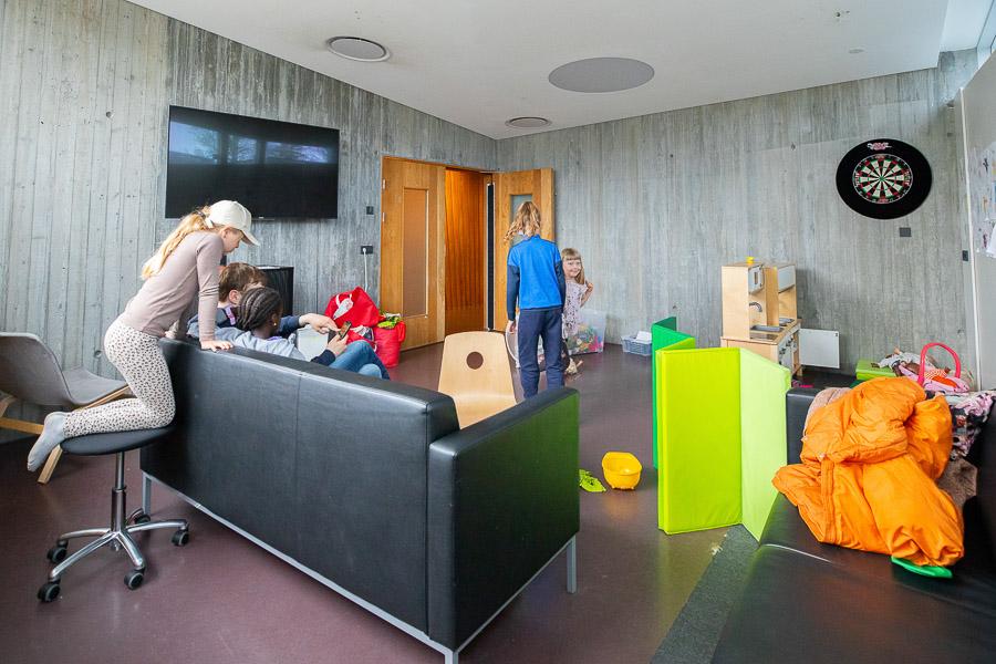 Black sofas, cushions, a toy kitchen and dartboard with children at play.