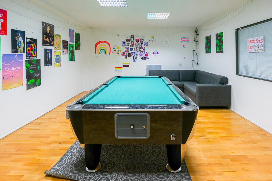 Room with pool table, corner sofa and posters on the wall. 