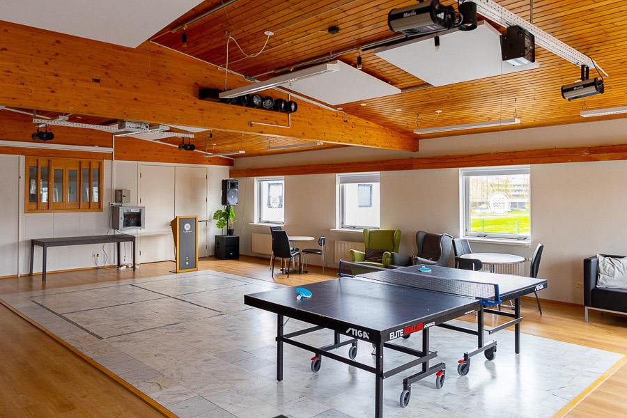 A hall with a ping-pong table, a couch, chairs, tables, and speakers.