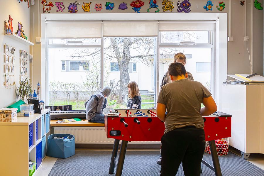 Children playing a soccer video game. In the background, children can be seen sitting on the windowsill. 