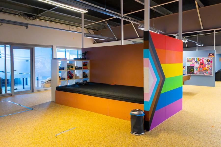 A large orange bench with a black cushion. A painted rainbow flag appears on the side.