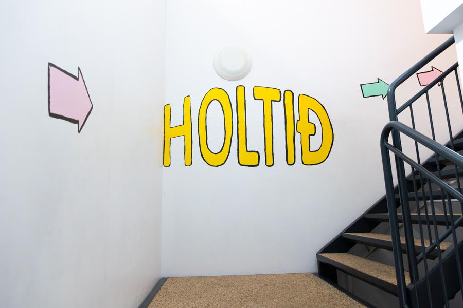 White staircase. “Holtið” is written on a wall next to an arrow pointing up the stairs. 