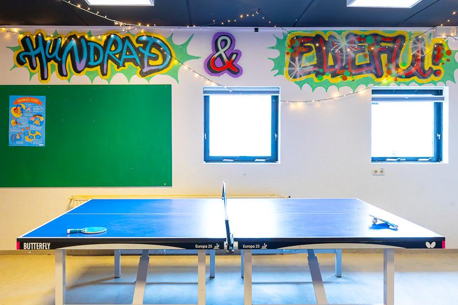 Ping pong table and decorated wall in the background with "Hundrað og ellefu" written on it. 