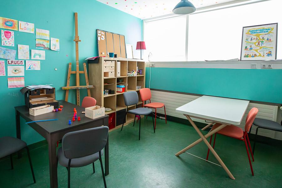 Green room with tables, chairs, shelf and stairs. 
