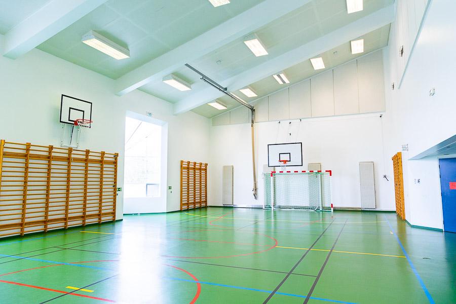 A sports hall with a slanted ceiling. A soccer goal, a basketball hoop, and jungle gyms. 