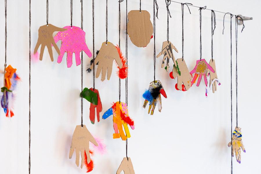 An artwork with colorful paper hands hanging on a wall.