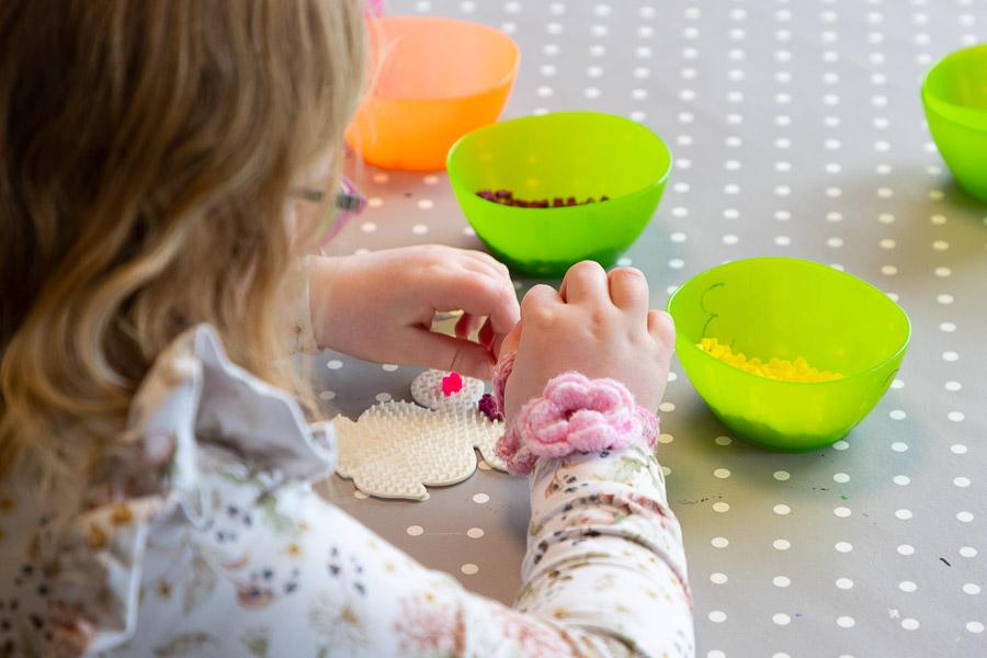A child sits with Perler beads at a table with a polka-dotted tablecloth.