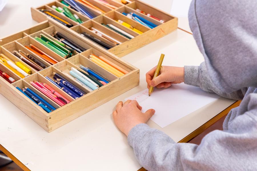 A child sits at a table coloring with colored pencils. Two boxes full of colored pencils on the table.