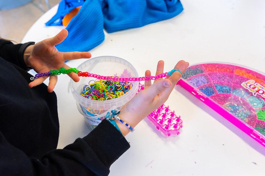A child sits at a table crafting with small, colorful rubber bands.