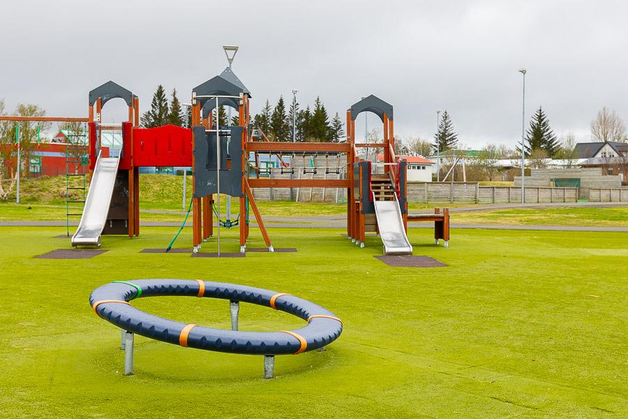 Outdoor play equipment on a grass field. A castle, a slide, and a ring.
