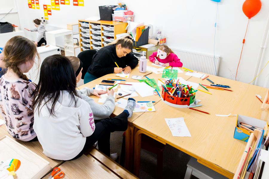 Children sit at a table with a recreation instructor, drawing and coloring. 