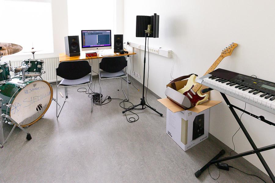 Room with a drum set, keyboard, guitars, speakers and computer screen on a table. 