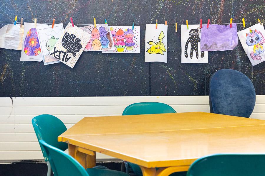Table and chairs. A black wall in the background with a string of children's artwork. 